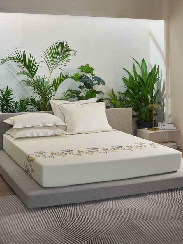 A bed with a white Boutique Bed Sheets and a plant on the floor.