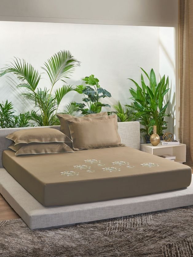 A bed with a brown bedsheet and a plant on the floor.