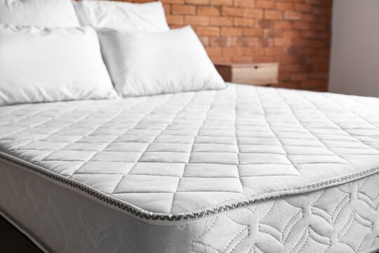 A grey mattress with neatly arranged white pillows on top.