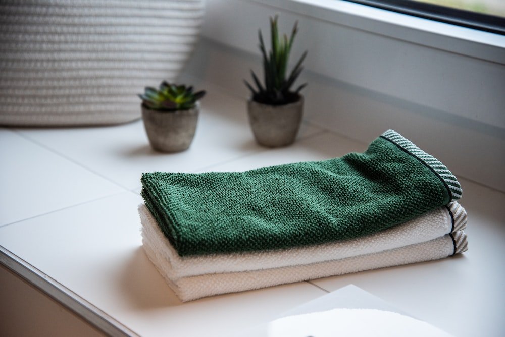 A stack of high-quality green and white towels neatly arranged on a window sill.